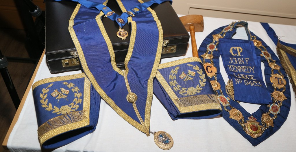Masonic artefacts: blue and gold regalia, jewellery and a gavel displayed on a table.